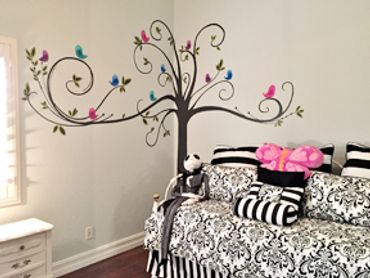 Decorative swirly tree with pink and blue birds. painted on wall corner behind black, white day bed.