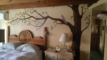 Brown tree with small green leaves on cream wall. Western headboard over bed.