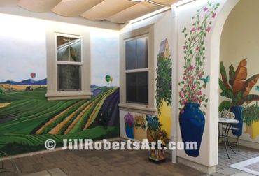 Exterior courtyard walls painted mural with wine country vineyards, potted plants, bird house