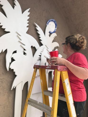 Jill Roberts mural artist painting cut out palm tree shapes for logo at The Colony HOA Murrieta, CA. 