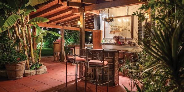 Exterior red tiled courtyard bar. lit up with palm trees and plants.