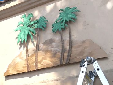 Cut out wood palm Trees and brown rocks painted mural mounted on wall at The Colony Murrieta, CA