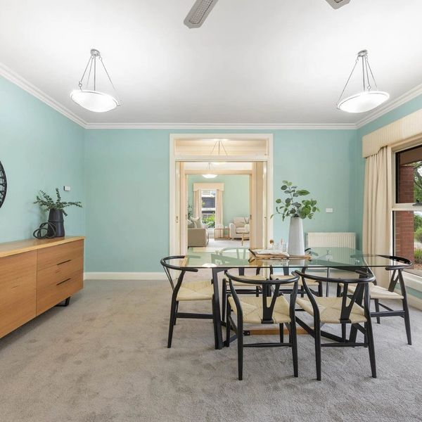 Modern dining room with glass table and black chairs on carpet.