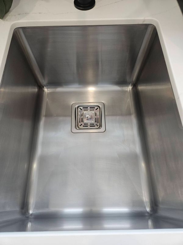 Shiny stainless steel sink with a square drain in a modern kitchen.