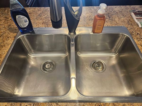Clean stainless steel double kitchen sink with soap bottles on each side.