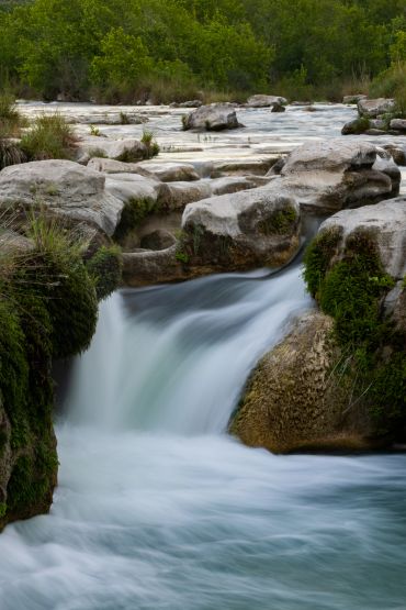 A serene waterfall flowing over mossy rocks surrounded by lush greenery.