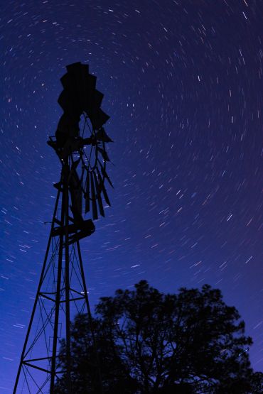 Silhouette of a windmill against a starry night sky with star trails.