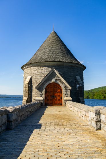 Stone tower with conical roof at the end of a bridge over water.