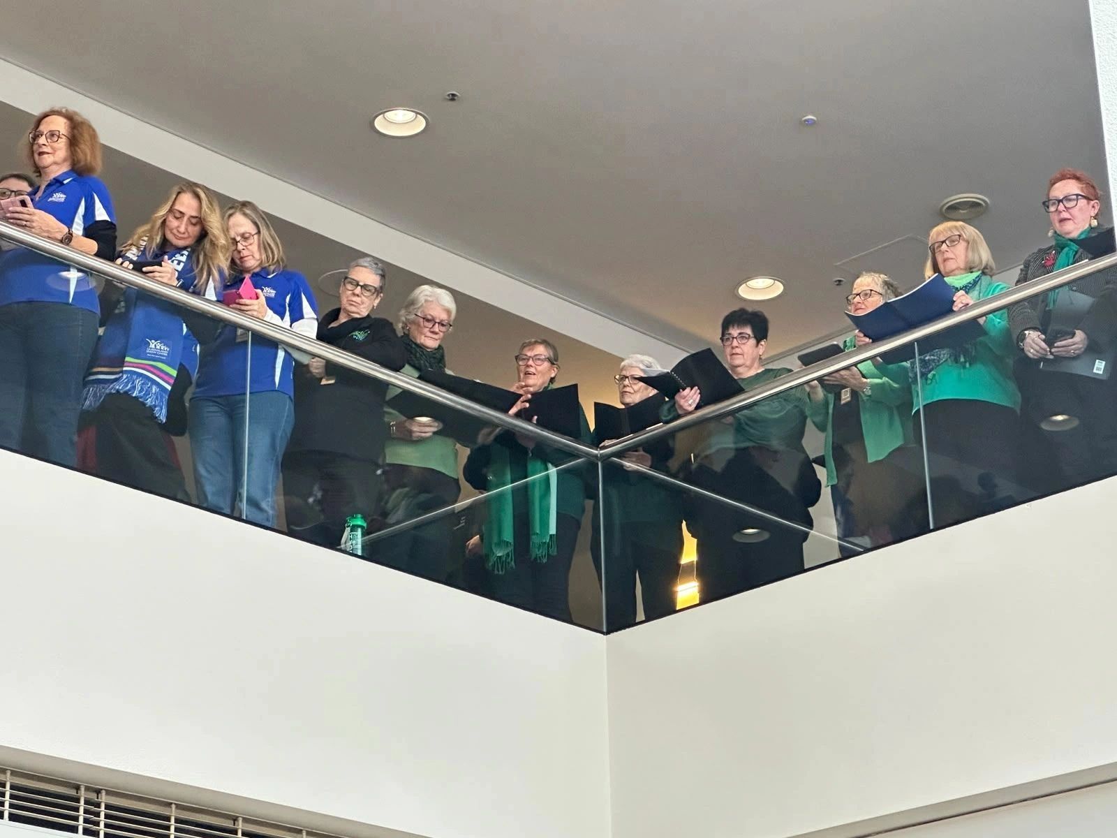 Women gathered on a balcony, some holding folders, others using phones.