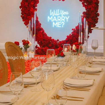 Elegant marriage proposal setup with red roses and a glowing "Will You Marry Me?" sign.