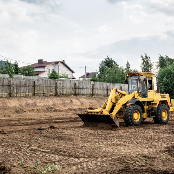 Yellow bulldozer land grading dirt field near residential houses.