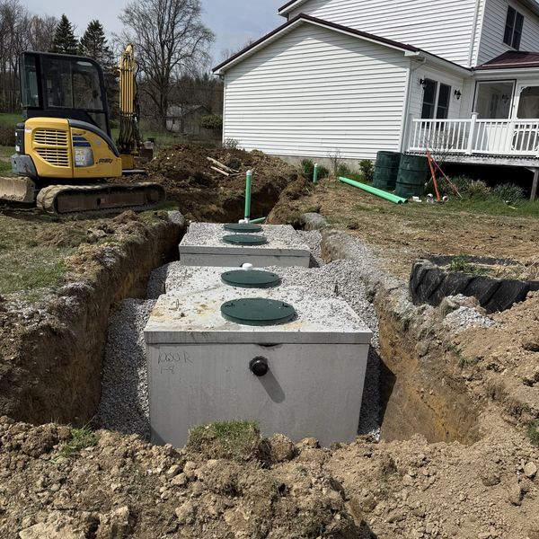 Concrete septic tanks being installed beside a house with an excavator nearby.