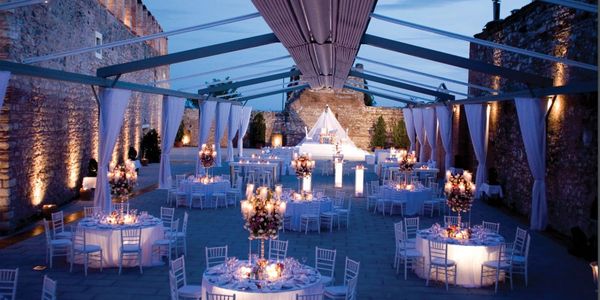Elegant outdoor dining space with open-beam canopy, chandeliers, and white draped curtains.