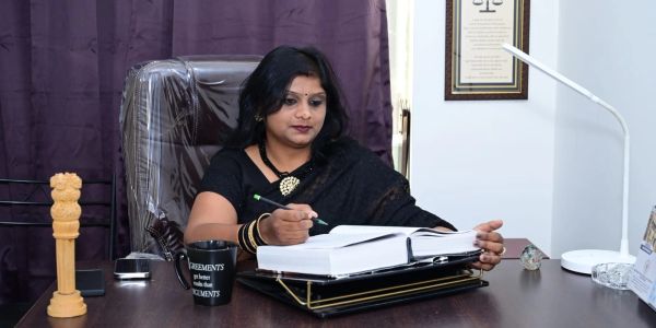 A woman in black saree working at a desk with documents and a mug.