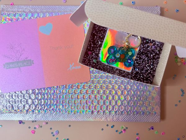 A colorful keychain in a box with thank you cards and holographic packaging.