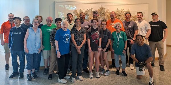 Group of diverse people posing indoors in front of a decorative wall panel.