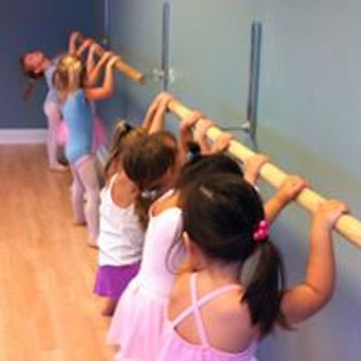 Young children practicing ballet at a barre in a dance studio.