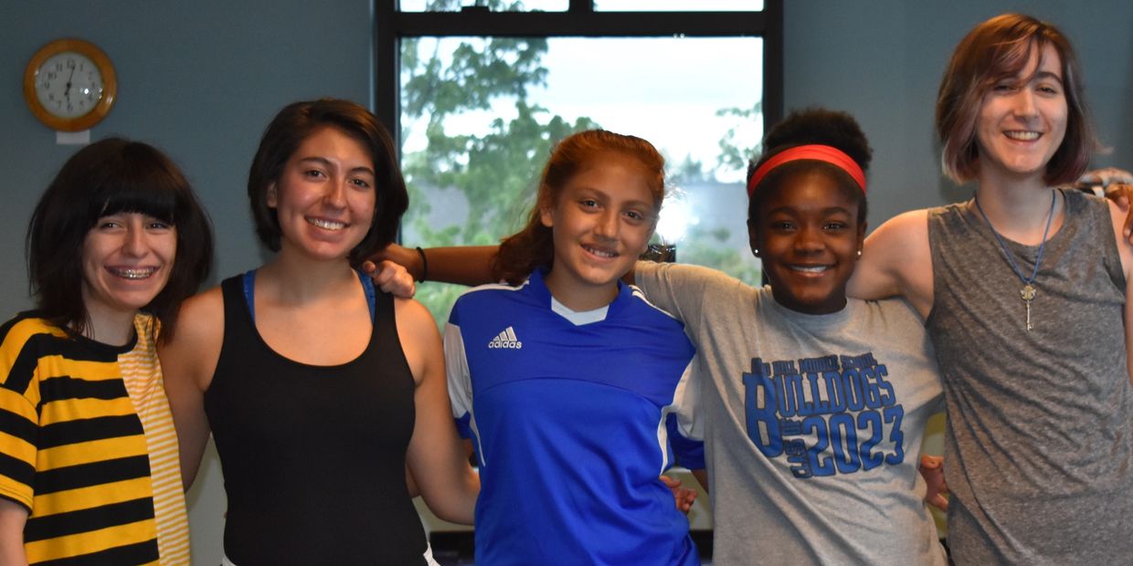 Group of five teens smiling together indoors.