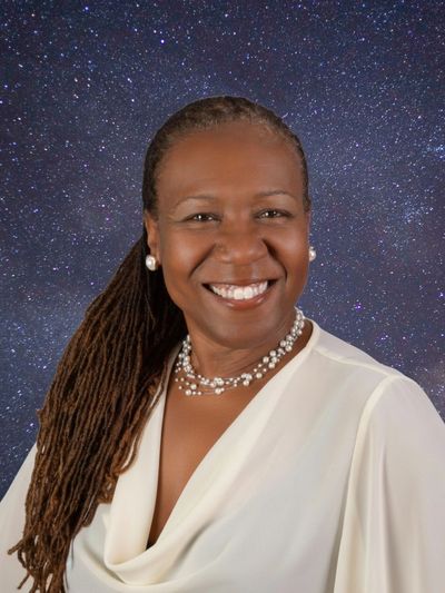 Smiling woman with long dreadlocks against a starry night backdrop.