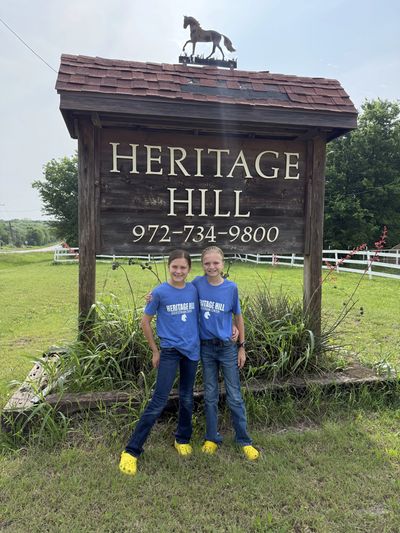 Two children in yellow Crocs stand happily in front of a Heritage Hill sign.