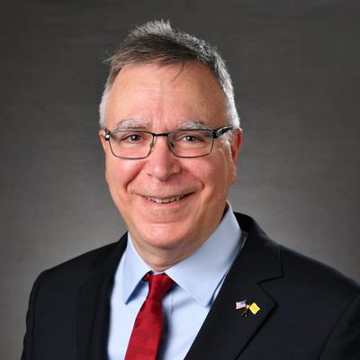 Smiling man in glasses wearing a suit with a red tie and lapel pins.