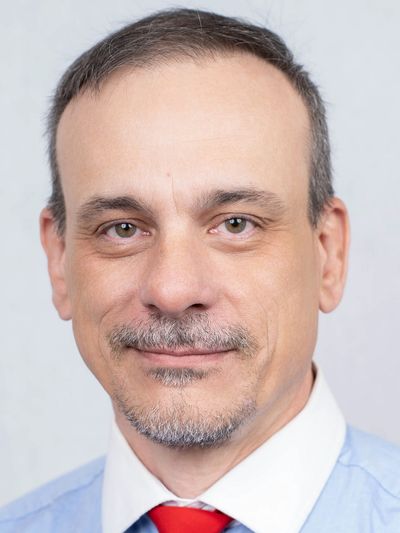 Portrait of a middle-aged man with a slight smile wearing a blue shirt and red tie.