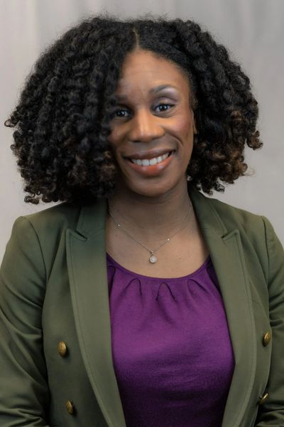 Smiling woman with curly hair wearing a green blazer and purple top.