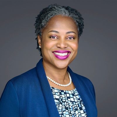 Professional woman smiling confidently in a blue blazer and pearl necklace.