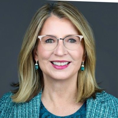 Professional woman with glasses smiling in a teal outfit.