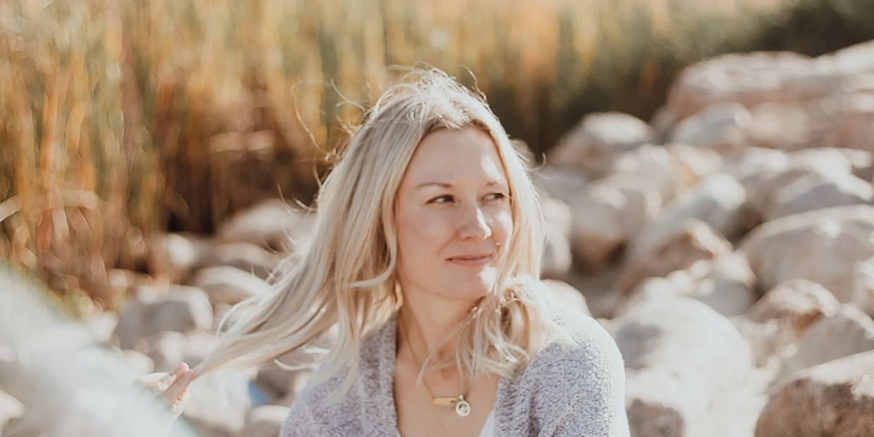 Woman with blonde hair outdoors, smiling slightly.