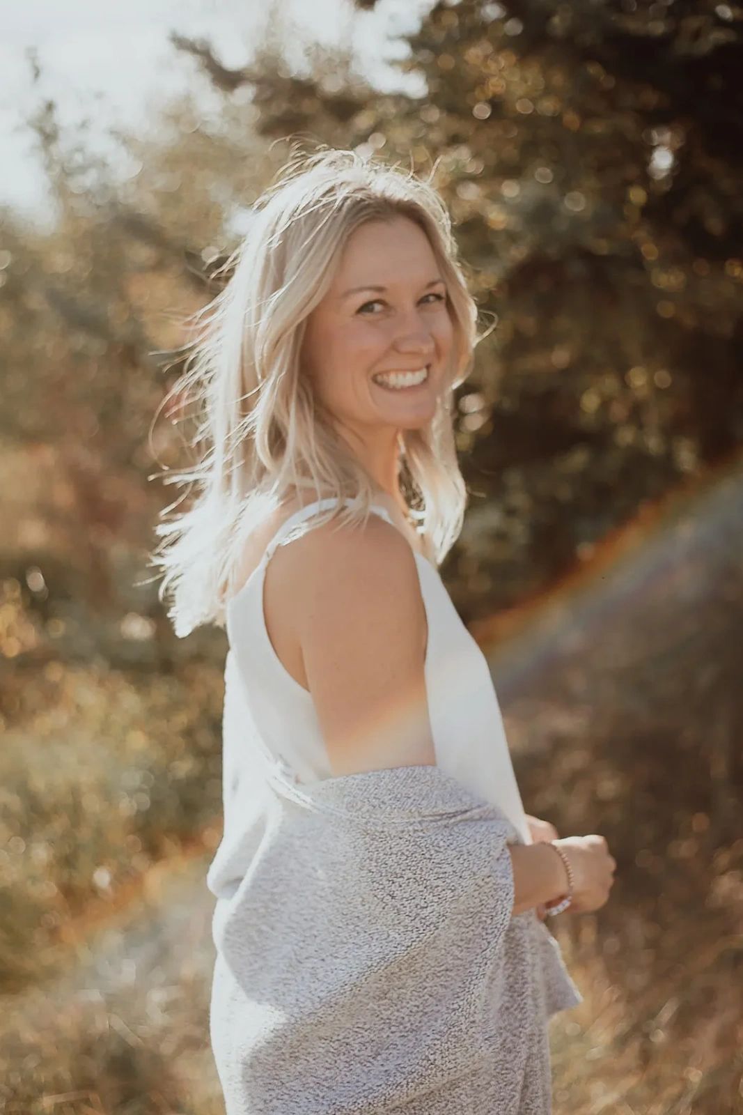Smiling woman in outdoor sunlight wrapped in a blanket.