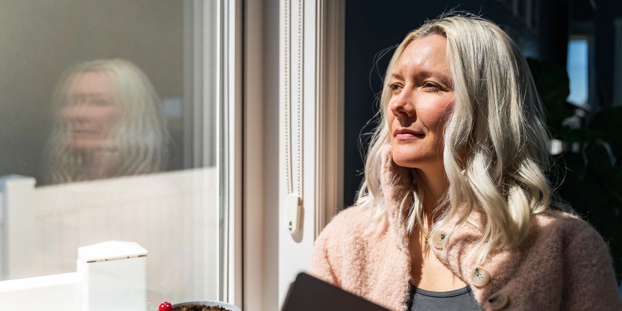 Woman gazing thoughtfully out window in soft sunlight.