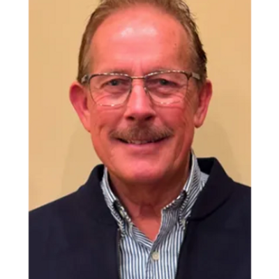 Smiling older man with glasses and mustache wearing a striped shirt and dark jacket.