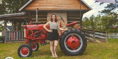 Woman standing by a red tractor near a wooden house.