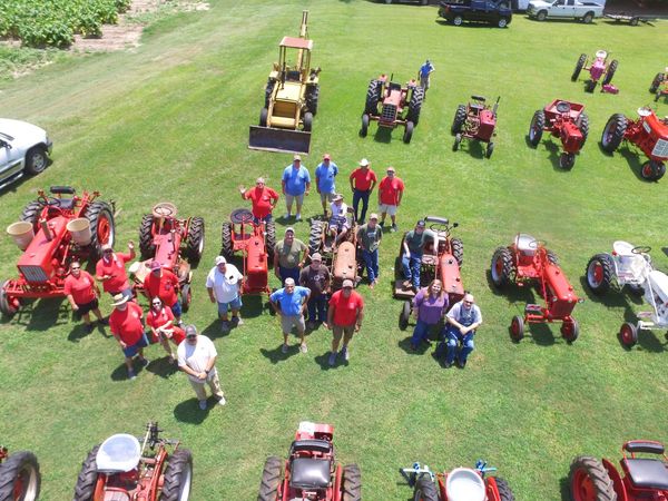 Group of people with vintage tractors on a grassy field.