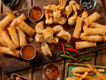 Assorted fried spring rolls and dumplings with dipping sauces on wooden boards.