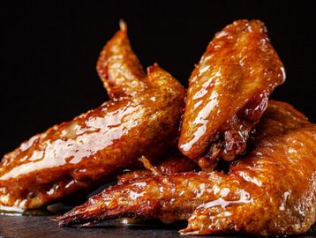 Glazed, crispy chicken wings stacked on a dark surface.