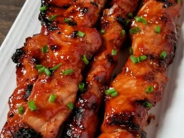 Grilled meat skewers garnished with chopped green herbs on a white plate.