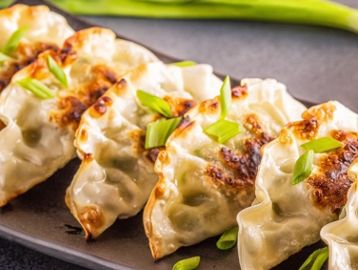 Plate of crispy pan-fried dumplings garnished with chopped green onions.
