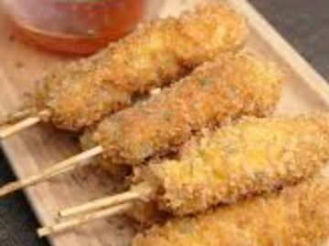 Four crispy fried skewers served with a red dipping sauce on a wooden tray.