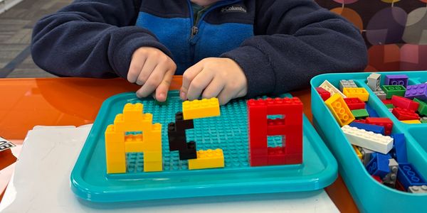 Child building a colorful LEGO figure on a blue baseplate.