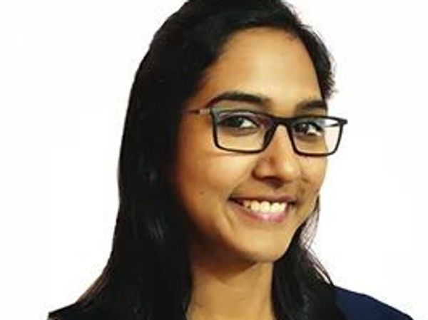 A smiling woman with glasses and long black hair wearing a dark blazer.