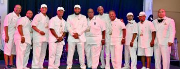 Group of men dressed in coordinated white outfits posing together.