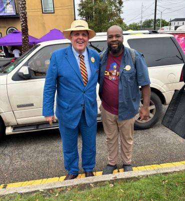 Two men smiling and posing in front of a white SUV outdoors.
