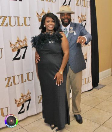 A couple dressed elegantly in front of a Zulu-themed backdrop.