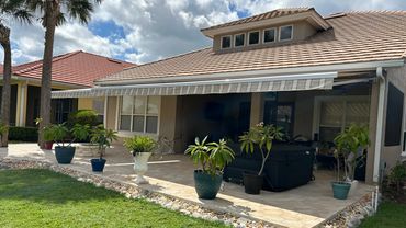 Backyard patio with plants and an awning under a cloudy sky.