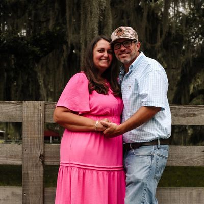 Couple smiling and holding hands outdoors by a wooden fence.