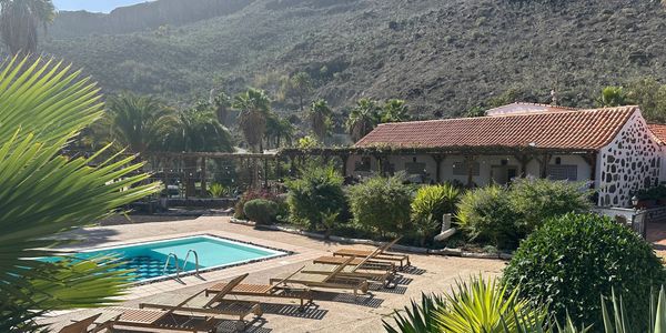 Outdoor pool with wooden lounge chairs at a rustic stone building.