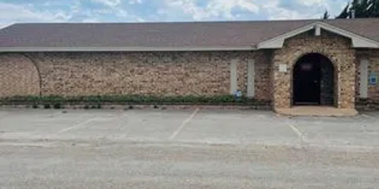 Empty parking lot in front of a brick building with arched entrance.