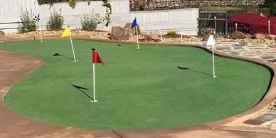 A backyard putting green with colorful flags near a lake and houses.
